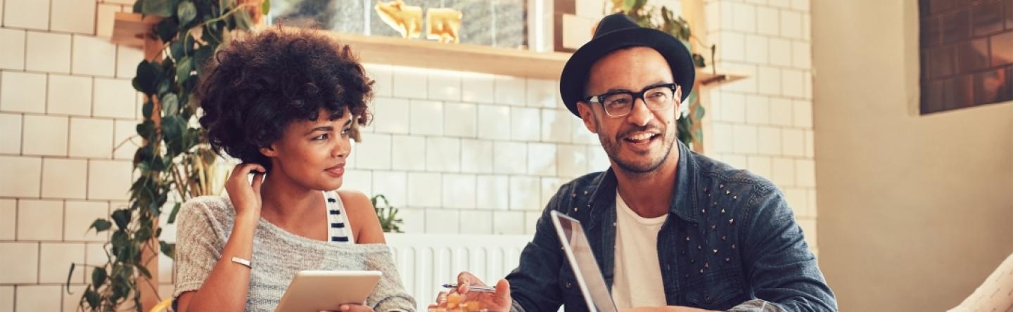 Vrouw en man zitten in gezamelijk overleg aan tafel.